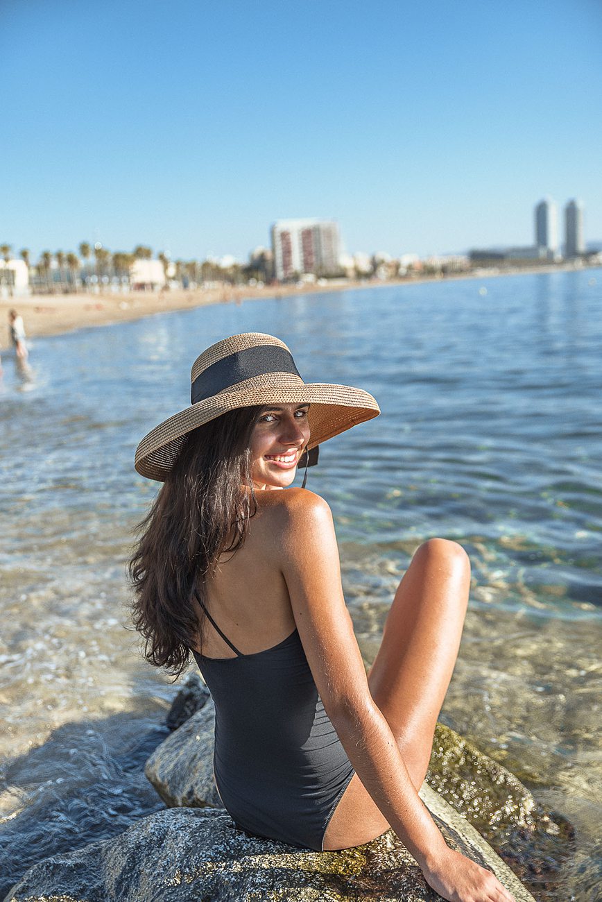 Zoe posing on rock on Barceloneta beach in black one piece swim suit